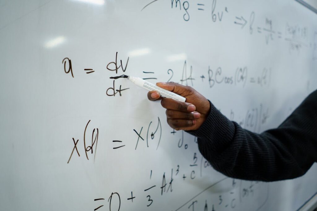 pexels photo 6209796 Close-up of hand writing equations on a whiteboard in a classroom setting.